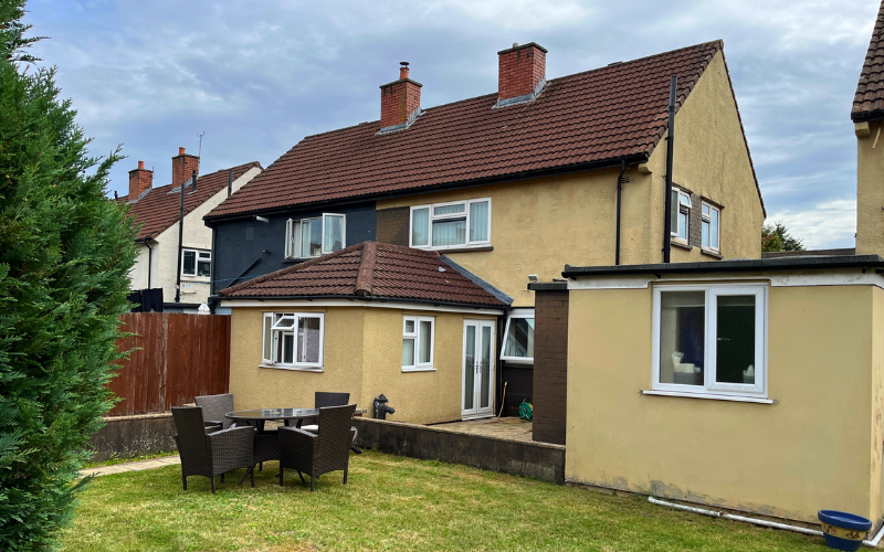 A view of the back of the home with the garden. There are some garden chairs and a table.